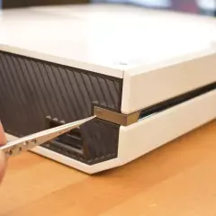 Dłoń z pęsetą zbliża się do przycisku parowania Xbox One, aby połączyć kontroler.