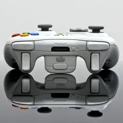 Biały kontroler Xbox 360 z kolorowymi przyciskami, odbijający się od czarnej powierzchni.