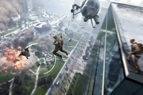 Skoczkowie w kombinezonach wingsuit spadają na miasto, podczas gdy helikopter i wybuchy tworzą chaos. Gra Battlefield 2042 wymaga odpowiedniego sprzętu.