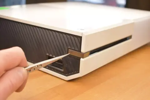 Dłoń z pęsetą zbliża się do przycisku parowania Xbox One, aby połączyć kontroler.
